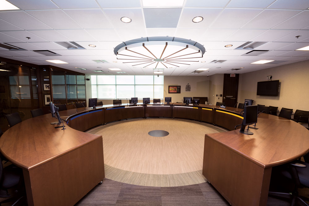 A circular courtroom with curved wooden desks arranged in a ring under a round ceiling light