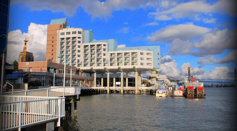 The Inn at the Quay hotel seen from the boardwalk, with the Fraser River, boats, and a bridge behind it